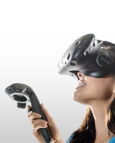 Technologie virtuální reality HTC Vive z roku 2016. Sada obsahuje náhlavní displej se sluchátky. Modelka drží "joystick" pro virtuální realitu, který detekuje a přenáší pohyb ruky do řídicího počítače. Foto HTC