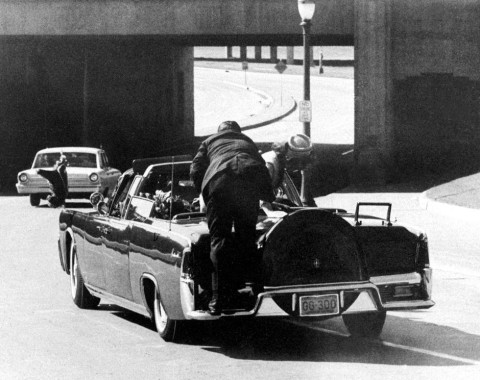 President John F. Kennedy slumps down in the back seat of the Presidential limousine as it speeds along Elm Street toward the Stemmons Freeway overpass after being fatally shot in Dallas on Nov. 22, 1963.  Mrs. Jacqueline Kennedy leans over the president as Secret Service agent Clinton Hill rides on the back of the car.  (AP Photo/Ike Altgens)